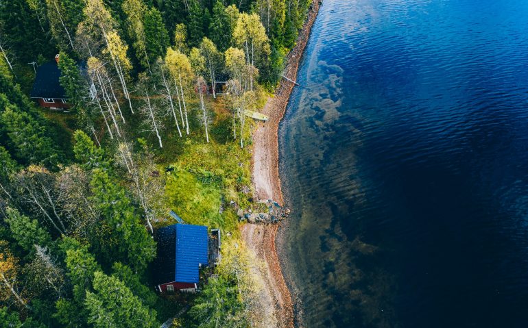 Aerial top view of log cabin or cottage with sauna in spring forest by the lake in rural Finland